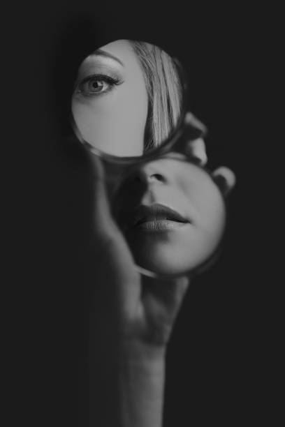 Woman looking at her eye and mouth in a small mirror artistic conversion stock photo