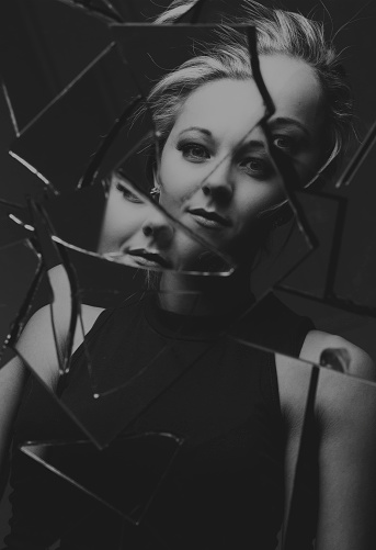 Woman looking at her face in shards of broken mirror pieces artistic conversion