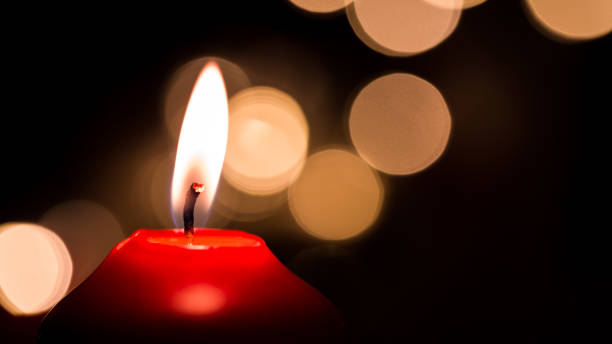 istock Burning red candle with golden colored bokeh and black background 902173108