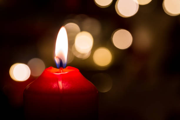 istock Burning red candle with golden colored bokeh and black background 902175640