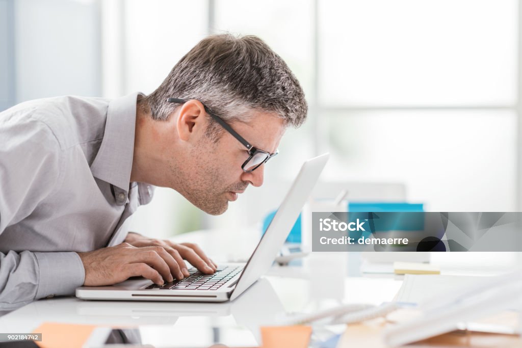 Workplace vision problems Businessman working at office desk, he is staring at the laptop screen close up and holding his glasses, workplace vision problems Computer Monitor Stock Photo