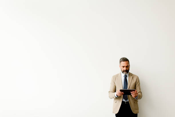 istock Handsome senior businessman with tablet by wall 902187184