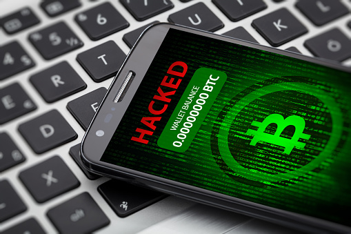 cryptocurrency theft comcept on smart phone screen. Big red hacked message and empty wallet. Phone on a laptop computer.