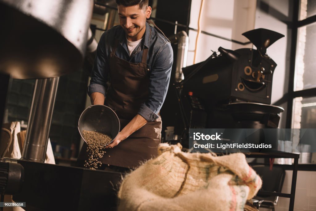 coffee roaster pouring coffee beans into roasting machine Coffee Roaster Stock Photo
