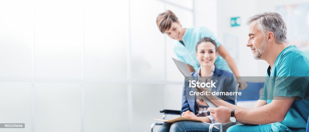 Doctors examining patient's medical records Professional doctor examining a patient's x-ray, a nurse is pushing her wheelchair, medical exams and healthcare concept Patient Stock Photo