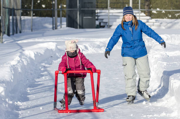 istock Young girl learning to ice skate using a helping accessory with mother besides 902231828