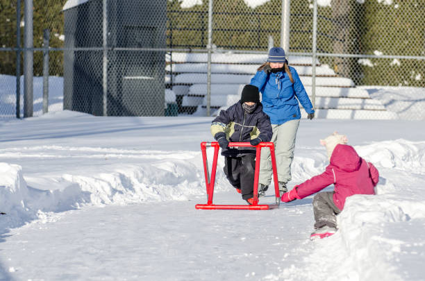 istock Mother teaching son how to ice skate while daughter is waiting sitting in snow 902234022