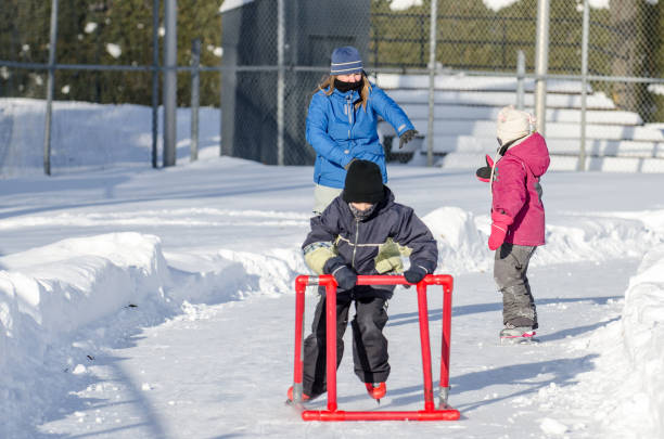 istock Mother teaching son how to ice skate while daughter is waiting sitting in snow 902234072