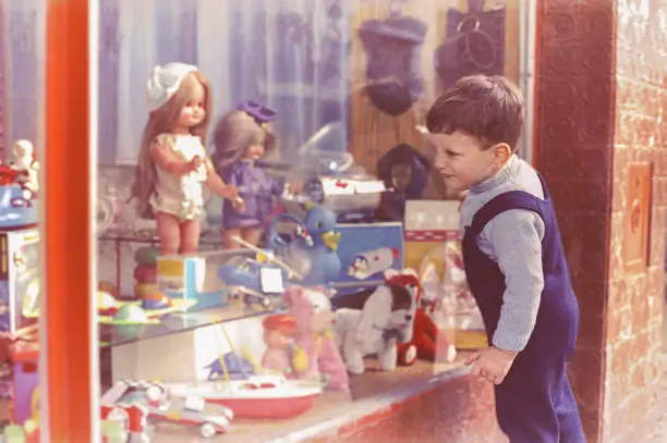 vintage photo from the sixties of a cute kid looking through the window of a toy's store