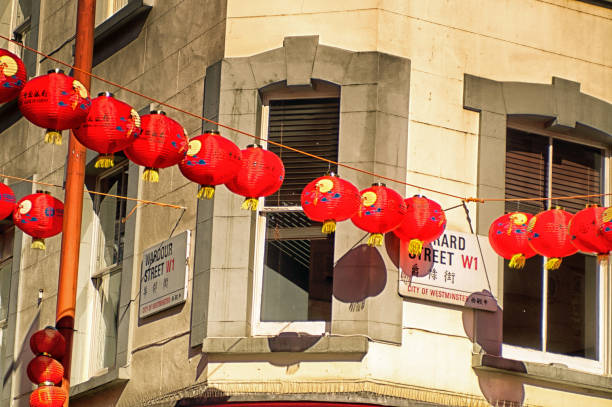 Chinese lanterns hung over Gerrard Street in China Town, London during Chinese New Year. They have Chinese text on them and are backlit by late afternoon sunlight.