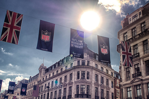 London streets with the union jack flag of the UK, the American flag, and a banner with the NFL - National Football League - logo hanging above them.
