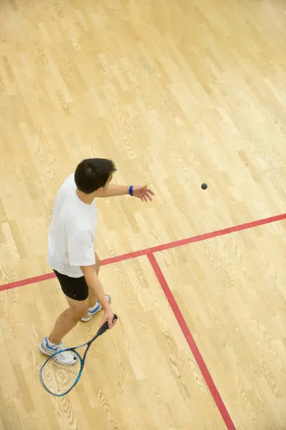 Squash player in action on squash court, back view.