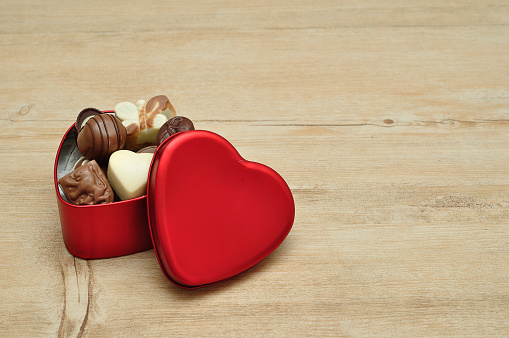 Round baked multicolored macarons lie in a red heart shaped box on wooden background