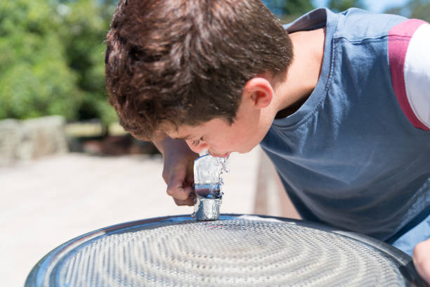 Close-up boy at water fountain enjoying a cool drink refreshing fresh water on summer day.