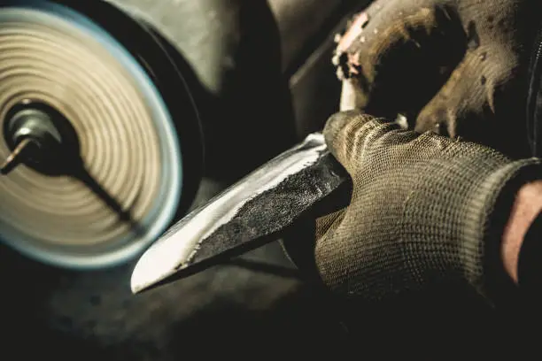 Blacksmith Holding a Knife in front of a Polishing Machine.