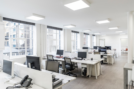 Desks and chairs in an empty office with telephones and office equipment, modern square lighting on white ceiling