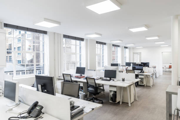 Large contemporary office environment with empty stations and electric ceiling lights Desks and chairs in an empty office with telephones and office equipment, modern square lighting on white ceiling neat office stock pictures, royalty-free photos & images