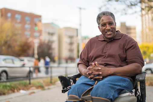 Portrait of the positive, optimistic disabled Black man, paralyzed veteran who sitting in wheelchair. Outdoor scene at the street in Bronx, New York City, USA