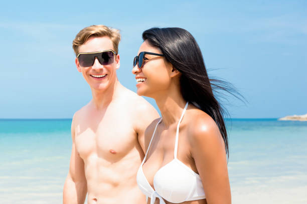 istock Young interracial tourist couple strolling along the beach 902338486