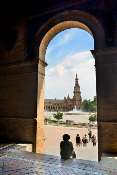 turismo masculino se sienta debajo de un arco de tranquilo en la expo de sevilla en un día caluroso de verano. - plaza de espana seville spain parque maria luisa fotografías e imágenes de stock