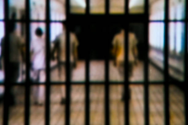 Behind the bars Taken this focused picture of the main entrance of a jail with people waking aware from it. Tried to capture the convict escorted by three security personal. prison stock pictures, royalty-free photos & images