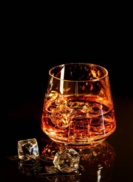 istock Whiskey with ice in glass on black background 902420752