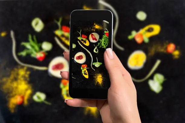 Closely image of female hands holding mobile phone with photo camera mode on the screen abstract gastronomy vanguard concept molecular cuisine. On a black background