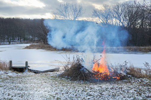 Piled up branches set on fire in a big bonfire. Winter and frost - frozen lake in forest