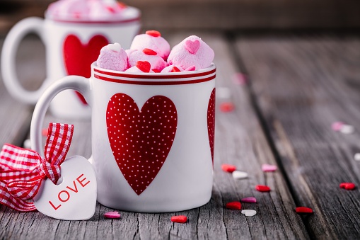 Hot cocoa with pink marshmallows in mugs with hearts on a wooden background for Valentine's day