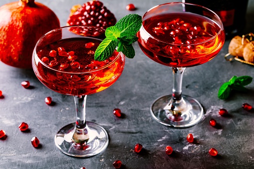 red cocktail with champagne and pomegranate seeds on rustic background