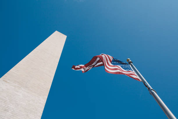 istock Low Angle View Of American Flag By Washington Monument Against Clear Sky 902449156