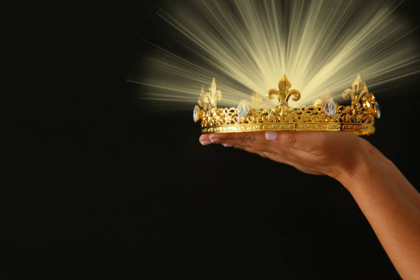 istock Woman's hand holding a crown for show victory or winning first place over black background with glitter overlay. 902460614
