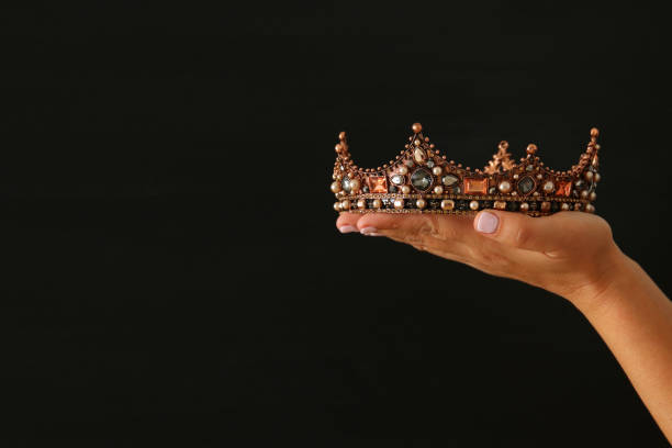 istock Woman's hand holding a crown for show victory or winning first place over black background. 902460622