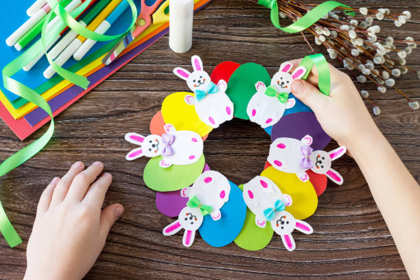 istock Children's Easter gift wreath with colorful eggs and Easter bunnies.  Paper, scissors, glue on a wooden table.Hand-made. Children's art project for children. Craft for kids. 902461894