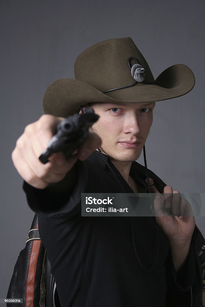 Bah-bah. Cowboy threatens revolver. Cowboy threatens revolver. Focus on face photo cowboy. Cowboy in black clothes and a leather jacket slung over his shoulder. Adult Stock Photo