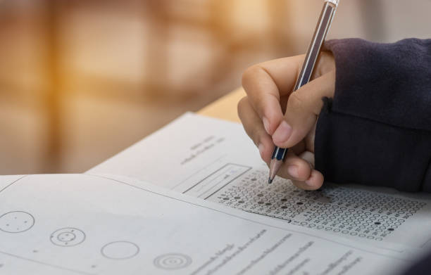 istock high school or university student hands taking exams, writing examination on paper answer sheet optical form of standardized test on desk doing final exam in classroom. Education  literacy concept. 902510884