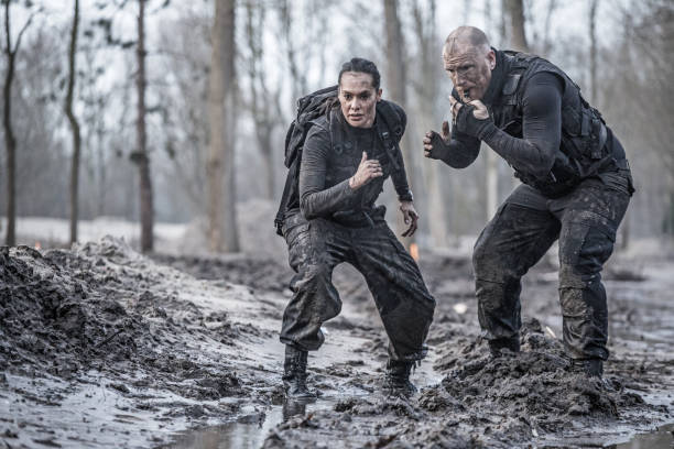 istock Redhead male drill instructor training beautiful brunette female soldier doing sprints outdoors in the mud 902517874