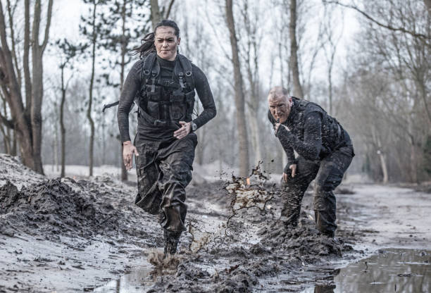 istock Redhead male drill instructor training beautiful brunette female soldier doing sprints outdoors in the mud 902519268