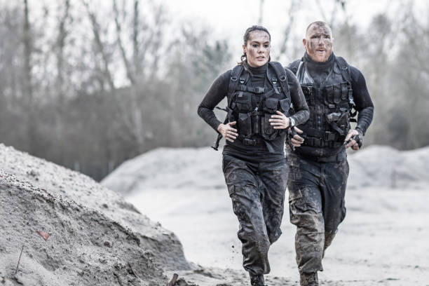 redhead male drill instructor running with beautiful brunette female soldier outdoors in the mud - mud run imagens e fotografias de stock