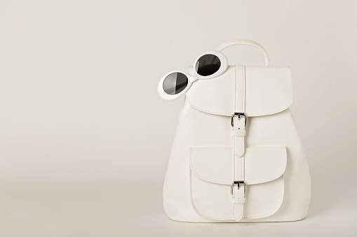 White female backpack and sunglasses on a white background. Selective focus.