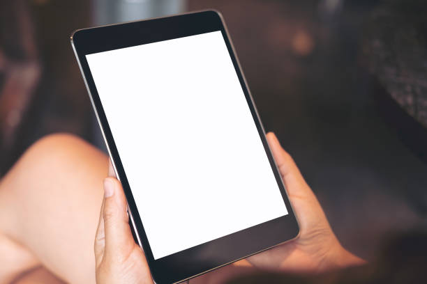 istock Mockup image of woman's hand holding black tablet pc with blank white screen on thigh in modern cafe 902559654