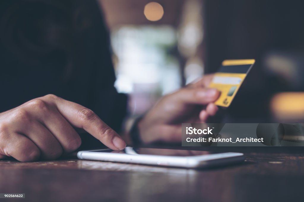 Closeup image of a woman's hand holding credit card and pressing at mobile phone on wooden table in office Adult Stock Photo