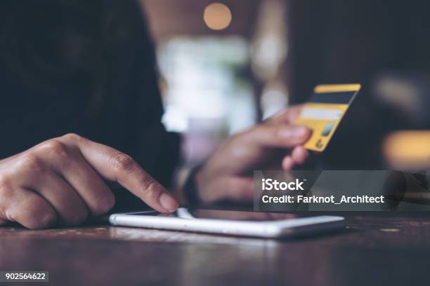 Closeup Image Of A Womans Hand Holding Credit Card And Pressing At Mobile Phone On Wooden Table In Office Stock Photo - Download Image Now
