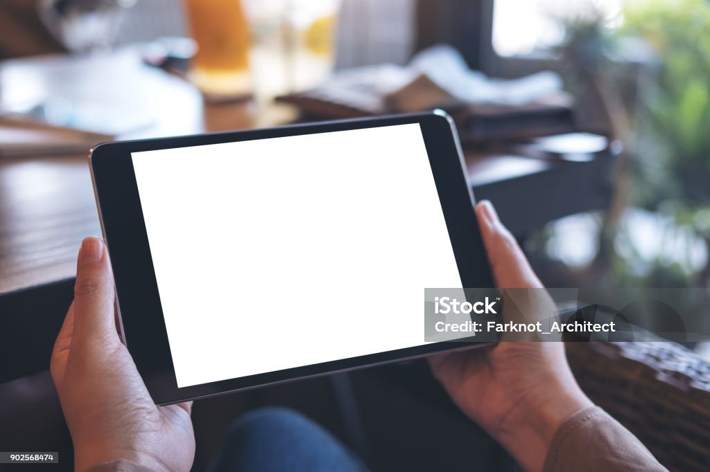 Mockup image of hands holding black tablet pc with white blank screen on wooden table background in cafe Digital Tablet Stock Photo