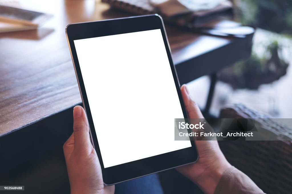 Mockup image of hands holding black tablet pc with white blank screen on wooden table background in cafe Digital Tablet Stock Photo