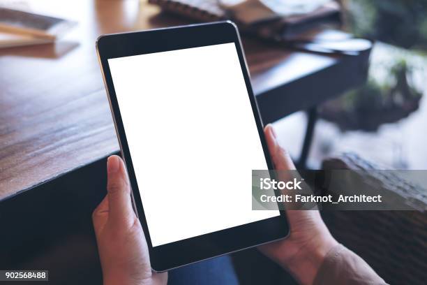 Mockup Image Of Hands Holding Black Tablet Pc With White Blank Screen On Wooden Table Background In Cafe Stock Photo - Download Image Now