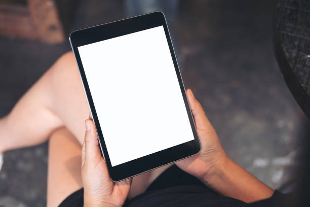 istock Mockup image of woman's hands holding black tablet pc with blank white screen on thigh with concrete floor background in modern cafe 902569292