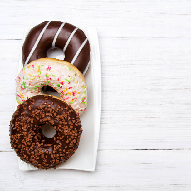 istock Tasty donuts with icing and chocolate on white wooden background, copy space 902575790