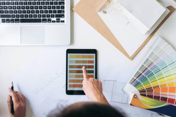 istock Two young women interior design or graphic designer working on project of architecture drawing with work tools and color swatches, colour chart in digital tablet at workplace 902592218