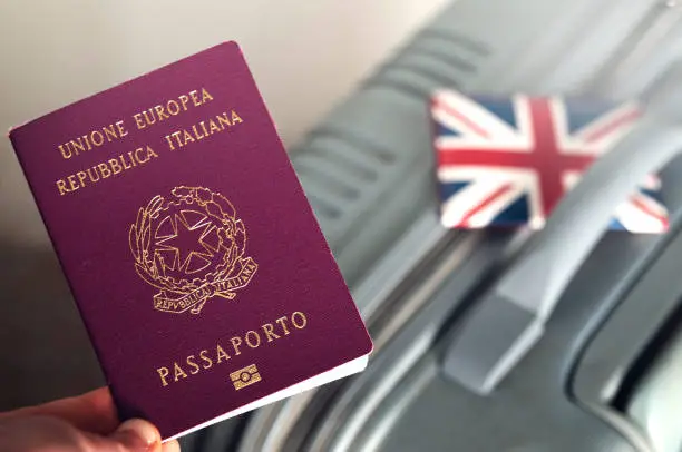 Photo of An italian passport holded over a suitcase with an english id holder on it